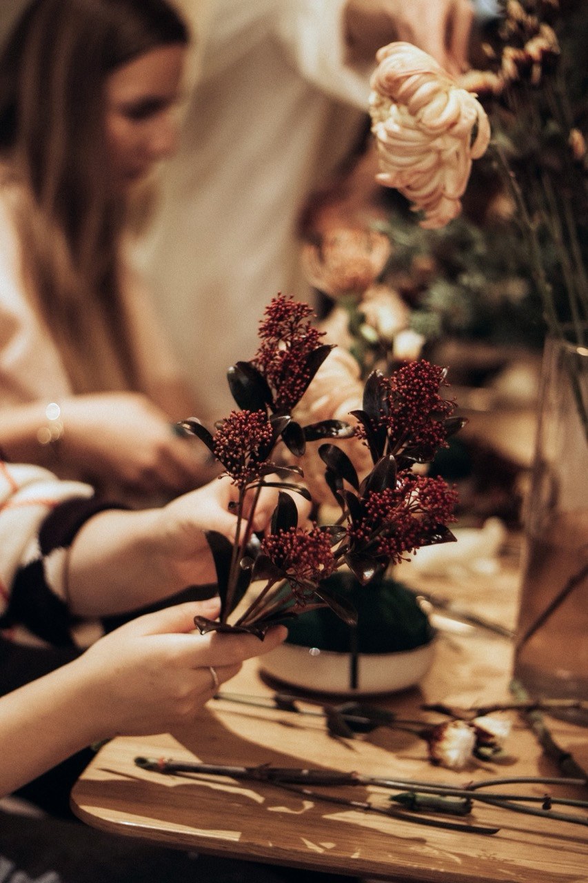 Hænder sætter blomster i et arrangement til en blomsterworkshop