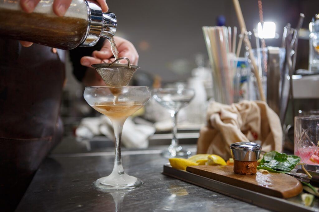 Cocktailkursus, si og glas Cocktail hældes gennem si ned i et glas